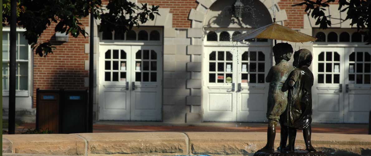 A statue of children with an umbrella and a brick building face. 